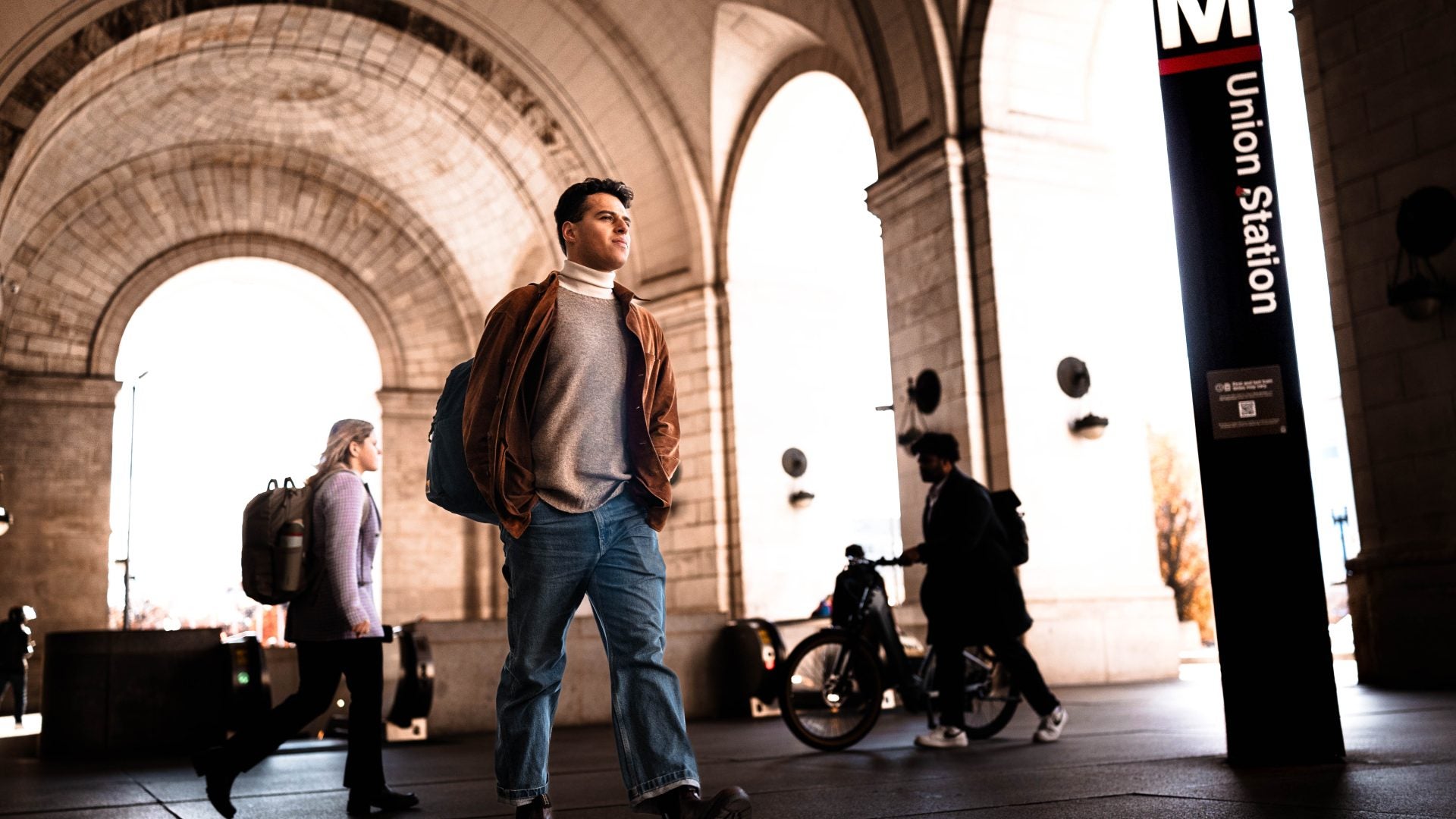 student walking under monumental stone arches at a bustling Union Station metro station