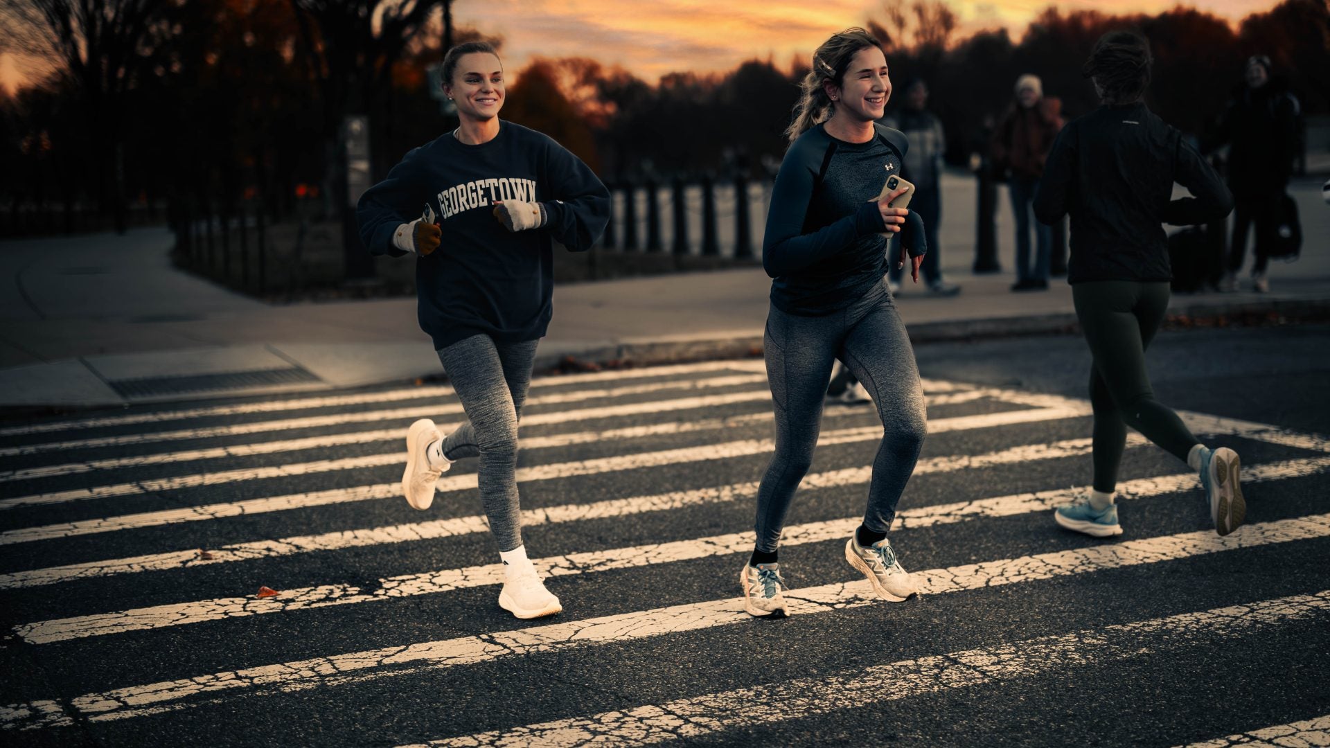 two female students running near the Lincoln memorial. One wears a Georgetown crewneck